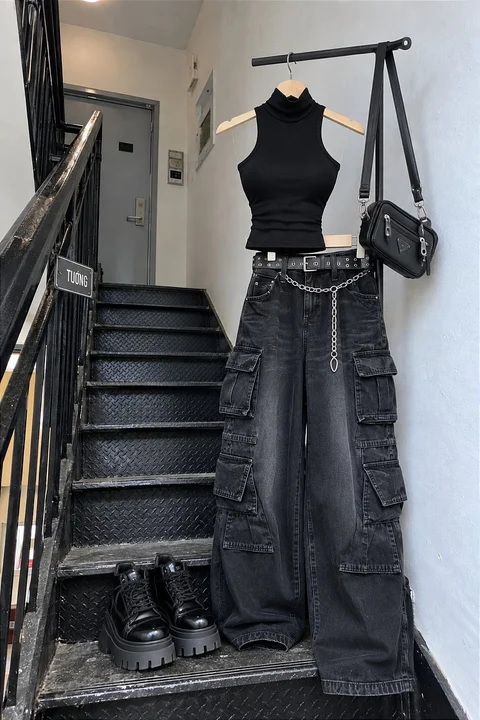 A black sleeveless top, wide dark jeans, a bag and shoes are displayed beside a metal staircase.